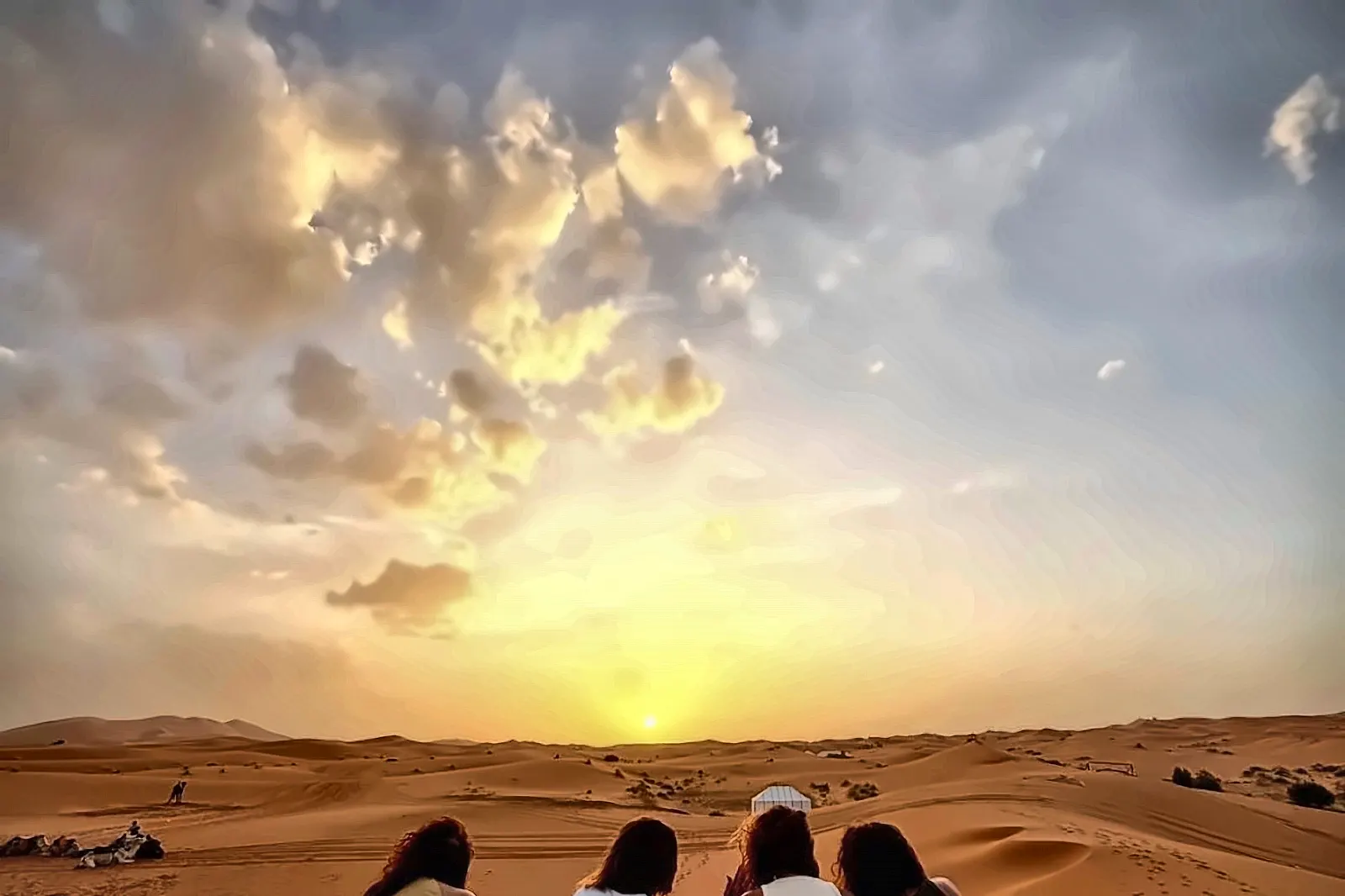 Un gruppo seduto sulla sabbia guarda il tramonto sulle dune